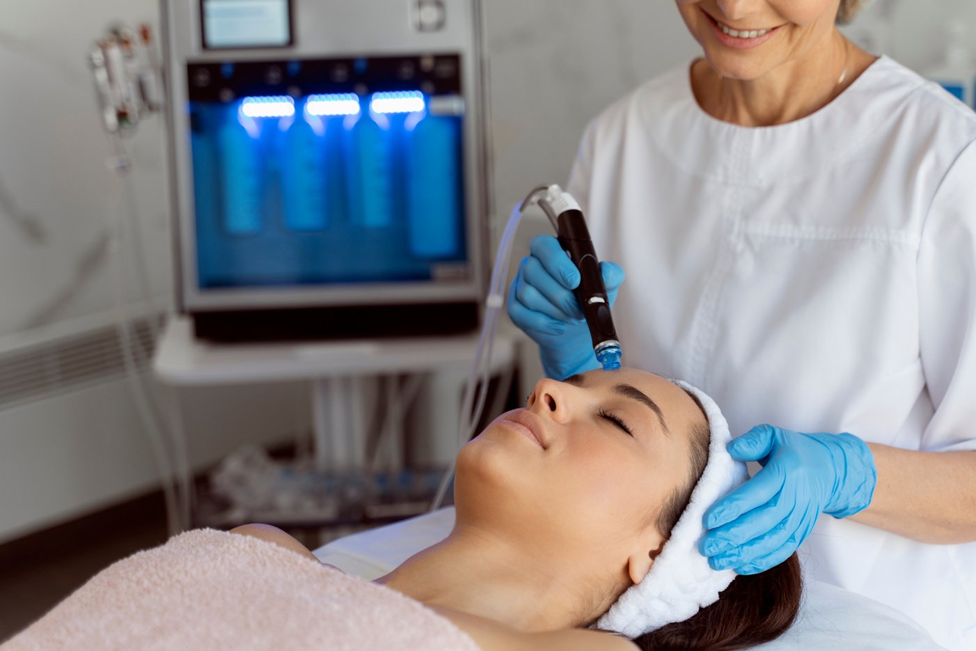 Professional female cosmetologist doing hydra-facial procedure in cosmetology clinic